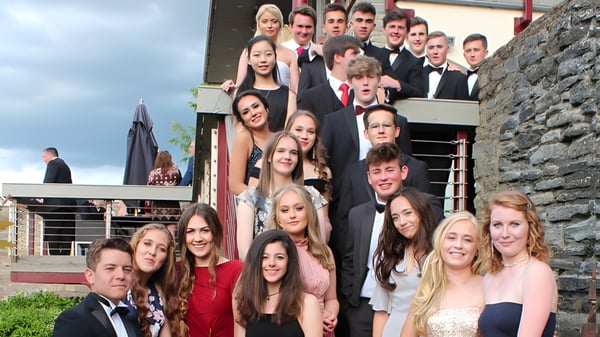 Un grupo de jóvenes adultos está de pie con ropa formal frente a un edificio de piedra en el campus de Bedstone College.