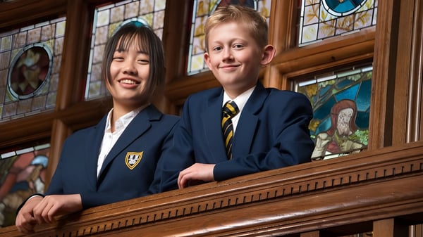 Dos estudiantes están de pie frente a una estructura de madera con ventanas de vidrio de colores en el campus de Bedstone College.