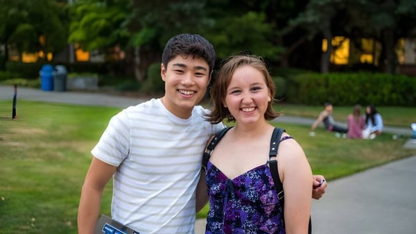 Dos estudiantes de la Bellarmine Preparatory School están afuera en un prado frente a edificios y árboles.