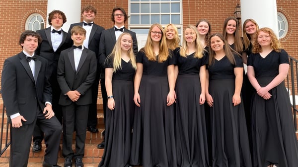 Un grupo de estudiantes de la Ben Lippen School está vestido formalmente frente a un edificio de ladrillo con ventanas de arco.