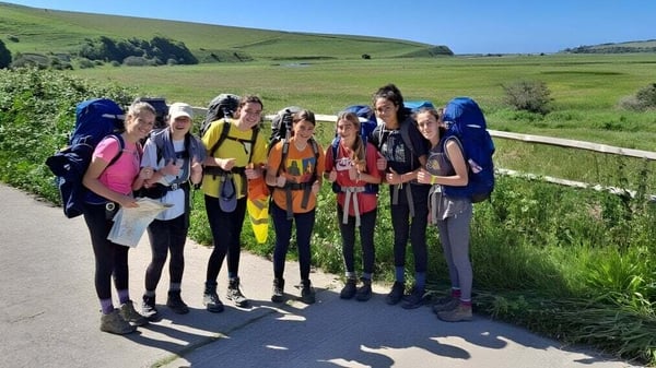 Un grupo de alumnas y alumnos de la Benenden School está de pie en un campo con montañas al fondo.