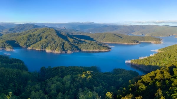Una toma aérea muestra un tranquilo paisaje de lago con bosques y montañas cerca de la Benowa State High School.