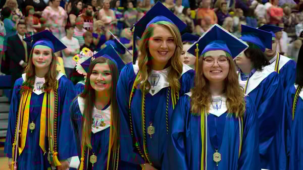 Graduados de la Bethlehem High School están en togas de graduación azules y doradas juntos en un auditorio lleno.