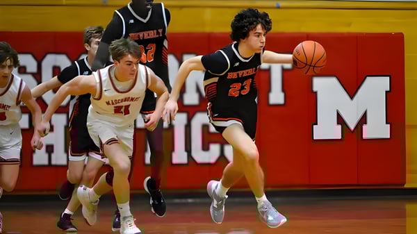 Estudiantes de la Beverly High School juegan un partido de baloncesto en el gimnasio escolar con un gran logo de ACM de fondo.