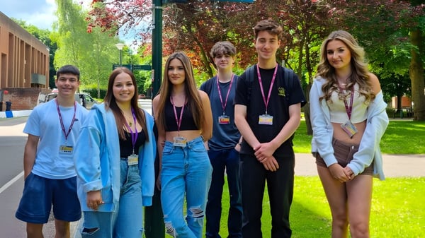 Estudiantes de Bexhill College están juntos en un área parecida a un parque con árboles y edificios al fondo.