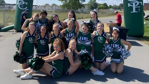 Un grupo de animadoras de la Billings Central Catholic High School posan al aire libre frente a un campo deportivo cercado.