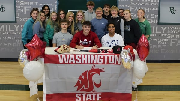 Un grupo de estudiantes de la Billings Central Catholic High School se reúne alrededor de un banner de la Washington State University para celebrar un éxito.