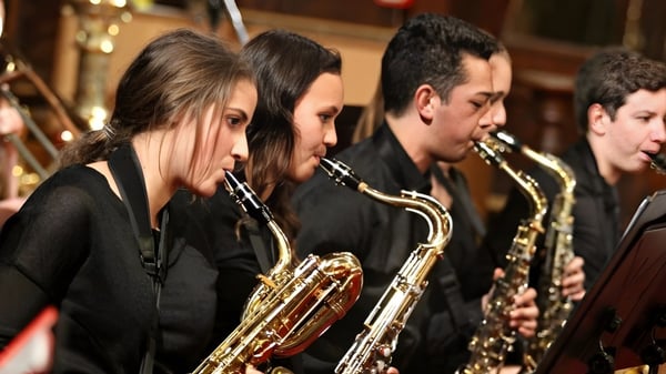 Un grupo de estudiantes de música del Birkenhead College toca diferentes instrumentos de metal en un escenario.