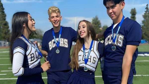 Cuatro estudiantes de la Birmingham Community Charter High School están juntos en sus uniformes deportivos azules en el campo deportivo.