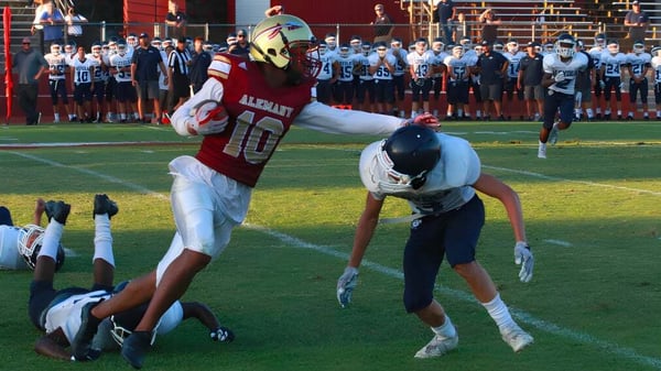 Un jugador de fútbol de la Bishop Alemany High School en camiseta roja realiza un tackle contra un oponente en el campo.