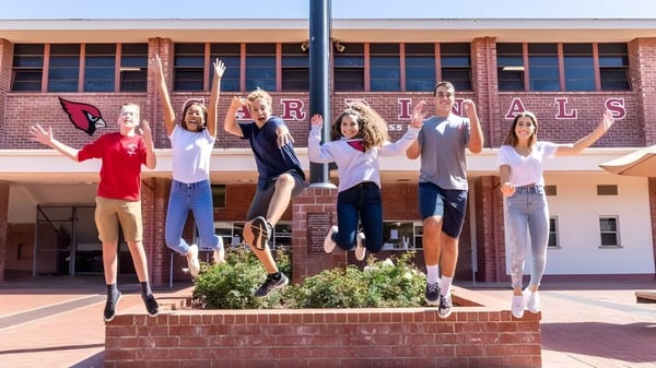 Un grupo de estudiantes de la Bishop Garcia Diego High School está en un muro de ladrillo frente a un edificio con la inscripción Rivals.