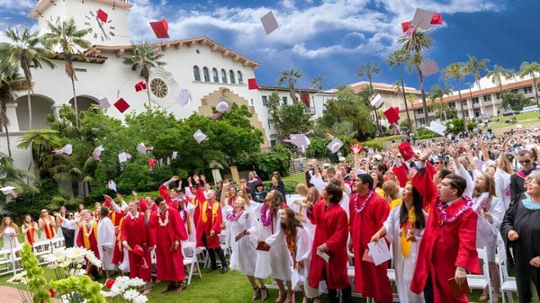 Los graduados de la Bishop Garcia Diego High School se reúnen frente a un edificio con palmas bajo un cielo azul.