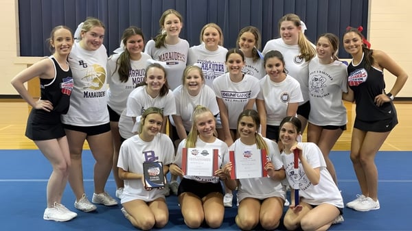 Un grupo de jóvenes atletas en uniformes deportivos posan en el gimnasio de la Bishop Guilfoyle Catholic High School.