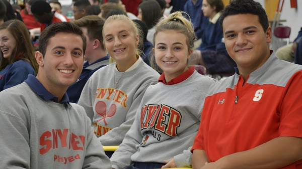Un grupo de alumnos de la Bishop J Snyder High School está sentado en una arena deportiva y lleva camisetas y sudaderas deportivas.