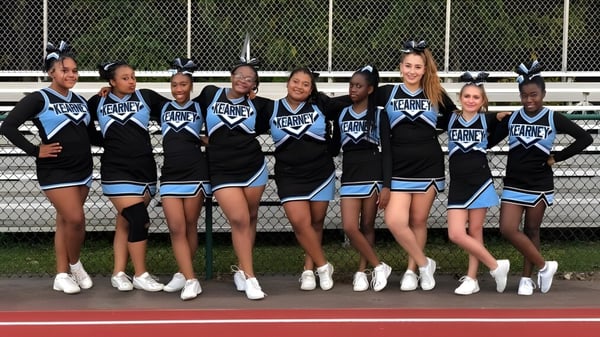 Un grupo de animadoras en uniformes uniformes está de pie en el campo deportivo de la Bishop Kearney High School.