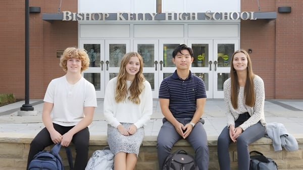 Cuatro estudiantes están sentados en un banco frente al edificio de la Bishop Kelly High School.