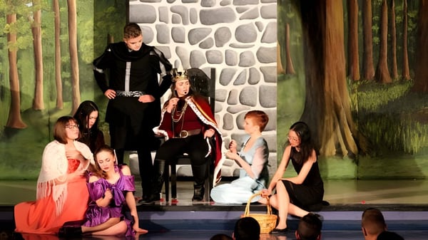 Estudiantes de la Bishop Mahoney High School ensayan una obra de teatro frente a una pared de piedra y un fondo de bosque.