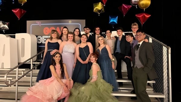 Un grupo de estudiantes de la Bishop O'Byrne High School posan en un escenario con globos de colores y decoraciones de fondo.