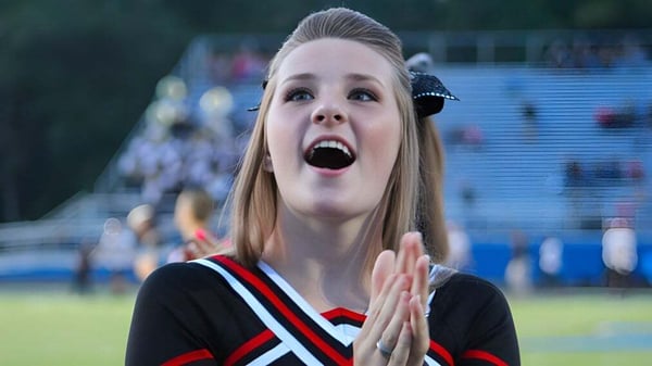 Una animadora de la Bishop Rosecrans High School está con expresión sorprendida en el campo deportivo frente a los espectadores.