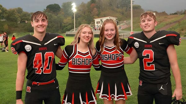 Cuatro estudiantes en uniformes deportivos negros y rojos de la Bishop Rosecrans High School están juntos en un campo deportivo.