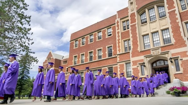 Un grupo de graduados de Bishop’s College School se encuentra frente a un gran edificio de ladrillo con arquitectura decorada.