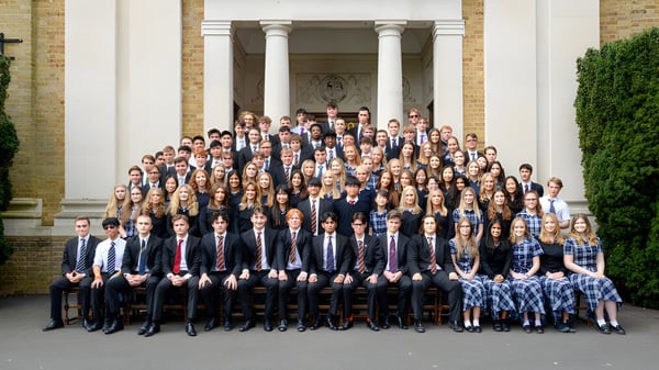 Un grupo de estudiantes del Bishop’s Stortford College posan con ropa formal frente a un edificio con columnas.