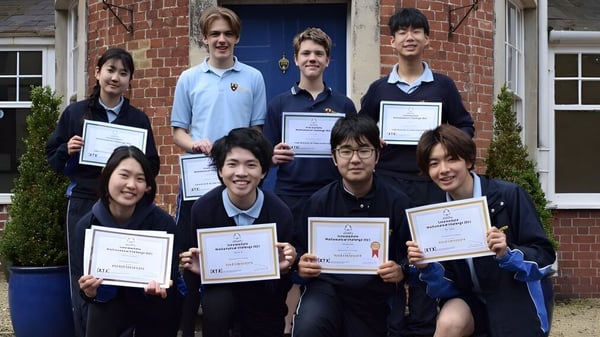 Estudiantes de Bishopstrow College están frente a un edificio de ladrillo sosteniendo certificados y premios.