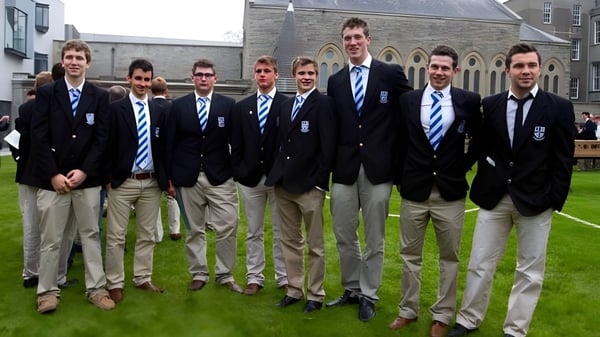 Un grupo de estudiantes del Blackrock College está de pie sobre un área de césped frente a un edificio de piedra.