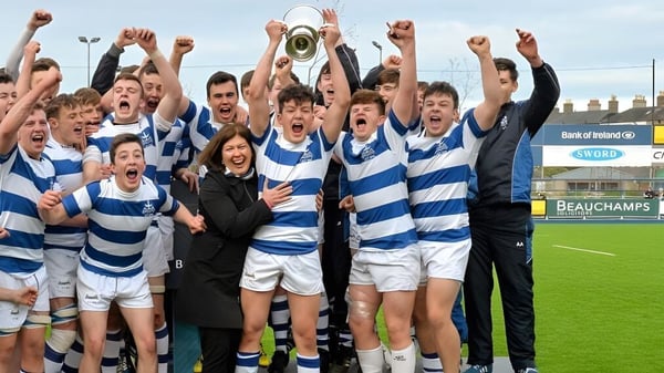 Un grupo de jóvenes jugadores de rugby celebra en el campo deportivo del Blackrock College su victoria con un trofeo.