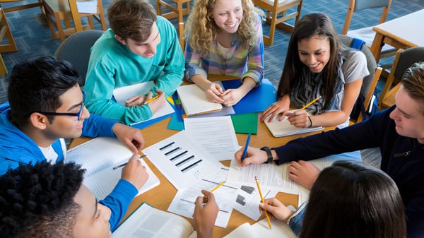Estudiantes de la Blackwater Community School trabajan juntos en una mesa con libros de texto y hojas de trabajo.
