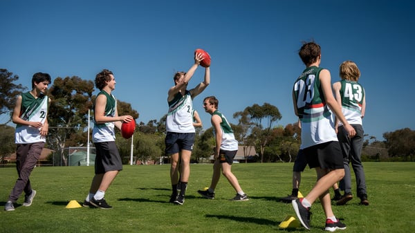 Un grupo de estudiantes juega al fútbol australiano en el campo deportivo de la Blackwood High School bajo un cielo despejado.