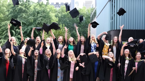 Graduados de la Bloxham School lanzan sus gorras al aire frente a edificios y árboles.