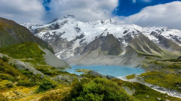 Vista de montañas cubiertas de nieve y un lago turquesa con vegetación verde frente a Blue Mountain College.