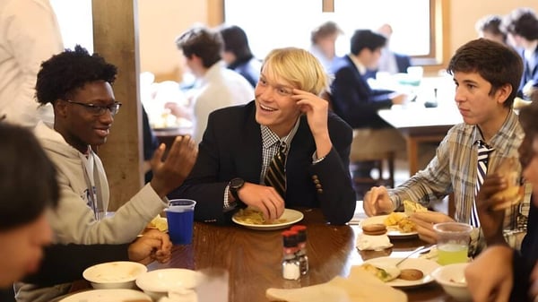 Estudiantes de la Blue Ridge School están sentados juntos en un comedor y conversan mientras comparten una comida.