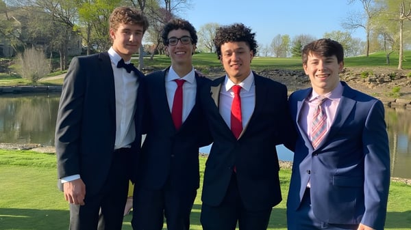 Cuatro estudiantes del Blue Valley School District están juntos en un parque con árboles y agua de fondo.