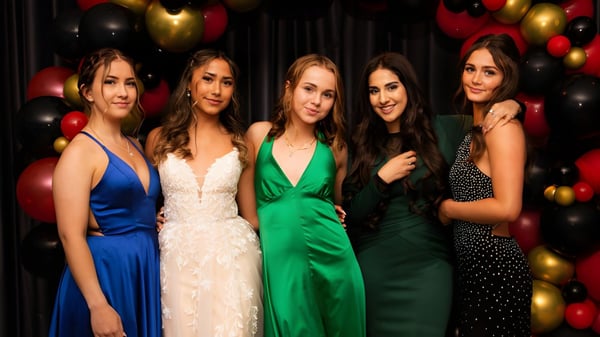 Cinco estudiantes de Bodmin College en ropa formal posan frente a una colorida pared de globos.