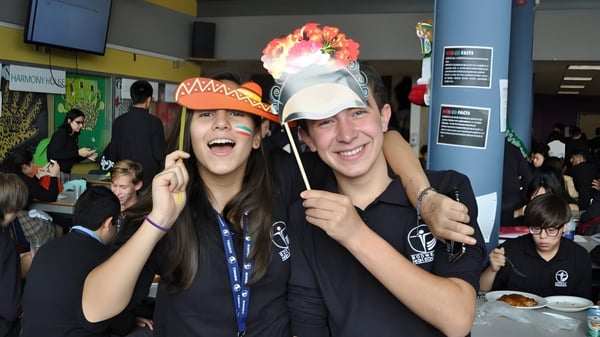 Dos estudiantes de la Bodwell High School sostienen coloridos requisitos en un interior lleno y sonríen.