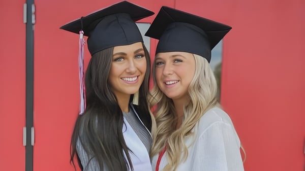 Dos estudiantes en ropa de graduación posan frente a un fondo rojo en el terreno del Bonneville Joint School District.