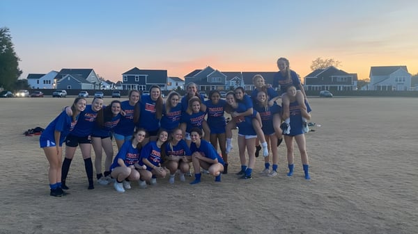 Un grupo de jóvenes atletas de Bootham School posan juntas en un campo de césped al atardecer.