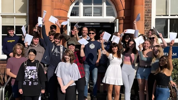 Estudiantes de Bootham School están frente a un edificio de ladrillo con ventanas de arco y sostienen carteles y pancartas.