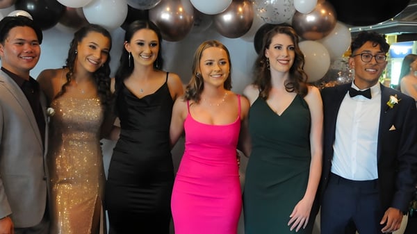 Un grupo de estudiantes bien vestidos posa frente a globos de colores en el campus de Bordertown High School.