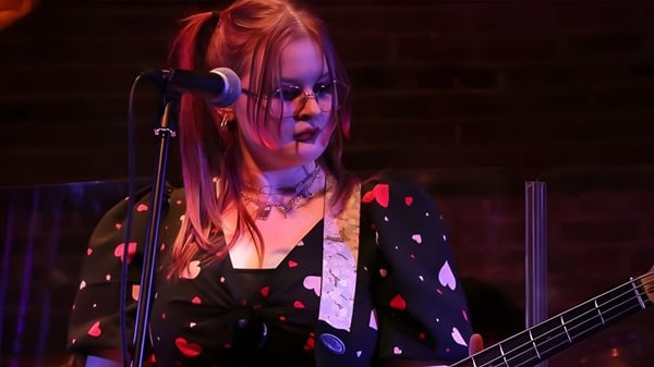 Una estudiante del Boston College toca la guitarra y canta en un escenario iluminado de colores.