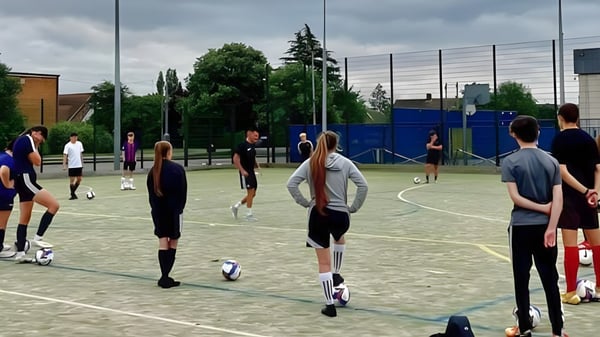 Un grupo de estudiantes del Boston College está en un campo de juego con una cerca y árboles de fondo.