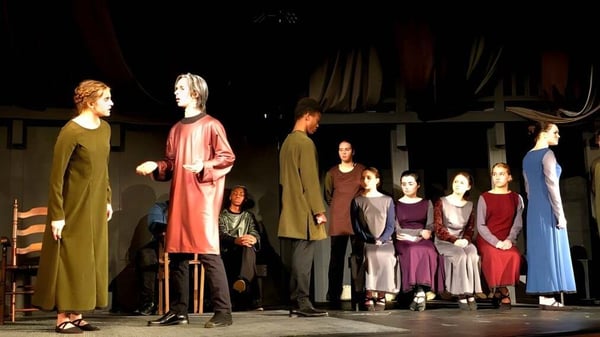 Estudiantes de la Boston Trinity Academy están en trajes coloridos en un escenario con decorado teatral.