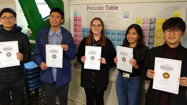 Cinco estudiantes sostienen certificados en un aula frente a la tabla periódica en el campus del Bosworth Independent College.