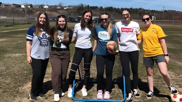 Un grupo de alumnas está de pie en un prado frente a una cerca y edificios en el campus de Botwood Collegiate.