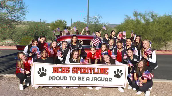 Un grupo de estudiantes de la Boulder Creek High School posan frente a un vehículo rojo y una pancarta de la Spirit Line.