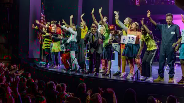 Estudiantes de Bournemouth Collegiate School presentan una animada actuación en el escenario con los brazos en alto en un fondo colorido.
