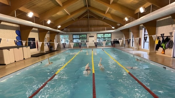 La piscina con techo de madera y marcas de carriles en el campus de Bournemouth Collegiate School con nadadores en el agua.