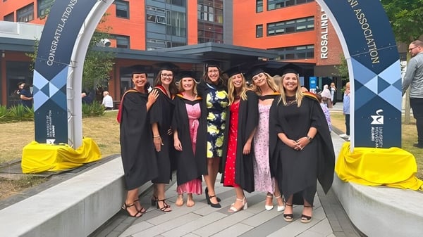 Estudiantes del Bournemouth & Poole College están en togas de graduación frente a un edificio universitario con pancartas en el fondo.